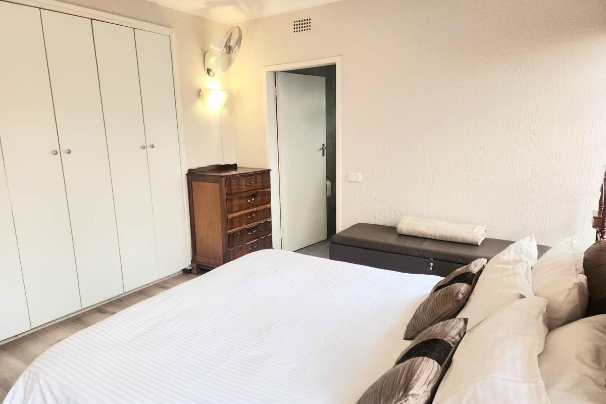 A well-lit bedroom featuring built-in cupboards, laminate flooring, and a wall-mounted fan, providing a functional and comfortable living space.