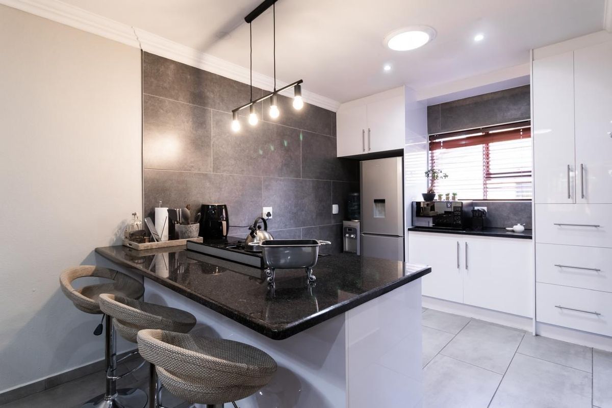 Modern kitchen featuring a breakfast bar, dark granite countertops, sleek white cabinetry, and a large format tiled feature wall.