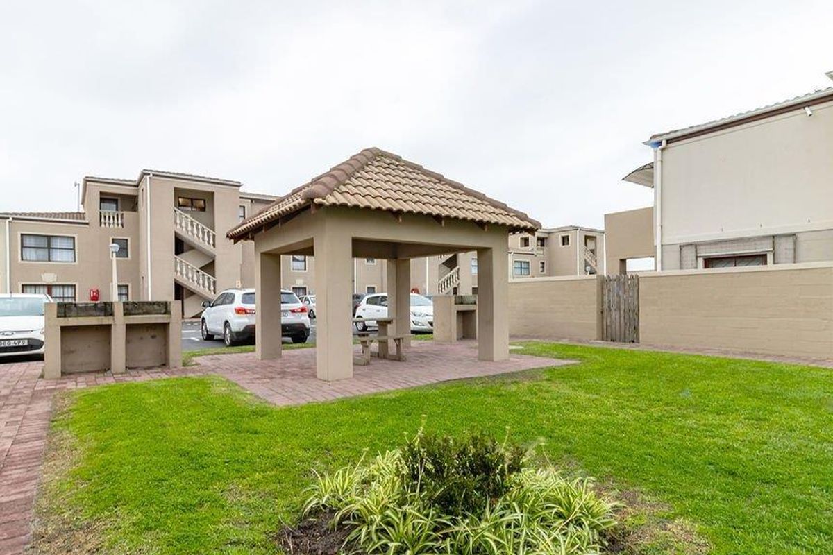 Communal outdoor area featuring a covered gazebo, built-in braai facilities, and well-maintained lawn within the apartment complex grounds.