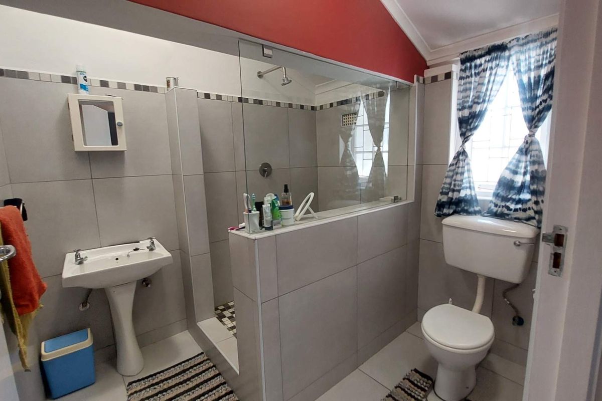 A functional bathroom featuring a walk-in shower with glass partition, pedestal basin, and toilet, finished with neutral wall tiles and a vaulted ceiling.