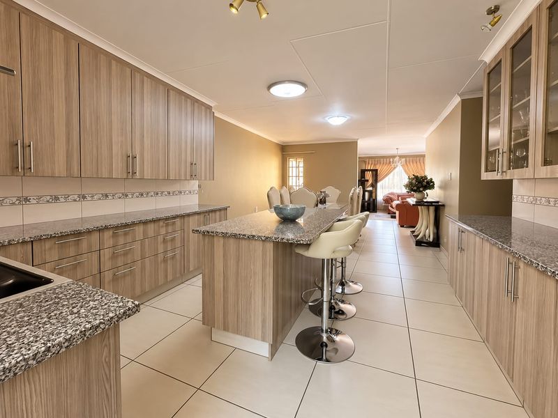 A spacious open-plan kitchen featuring modern laminate cabinetry, granite countertops, a central island, and light ceramic floor tiles, flowing into the dining and living areas.