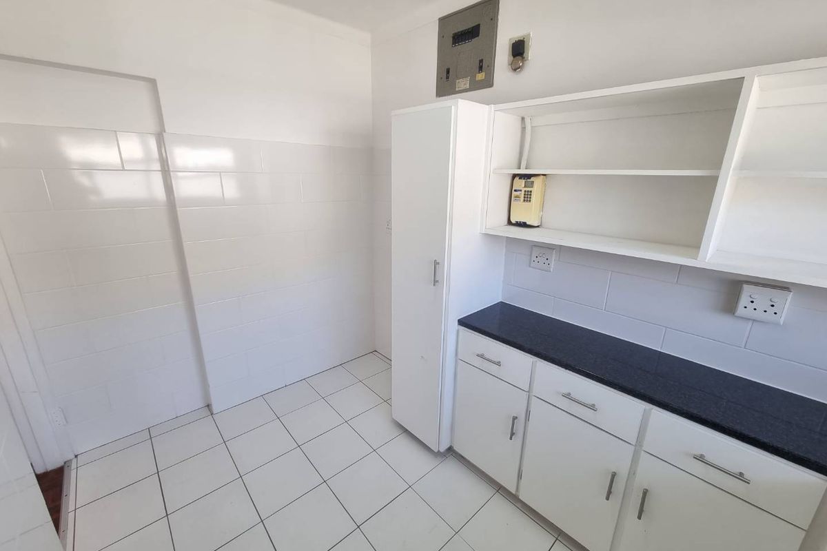 A clean, functional kitchen area featuring white cabinetry, dark stone countertops, tiled flooring, and a tiled splashback, providing a blank canvas for customization.