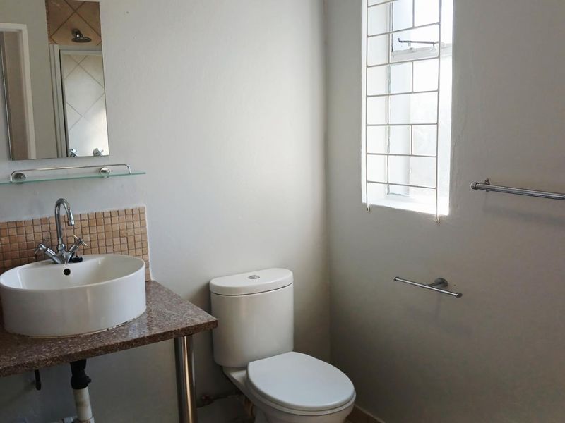 A functional bathroom featuring a vessel sink on a granite vanity, mosaic splashback, and a standard toilet with security bars on the window.