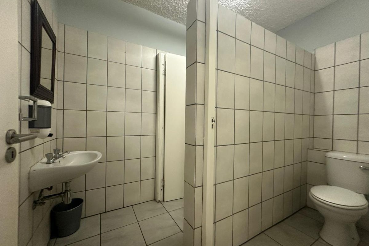 A functional office restroom featuring tiled walls and flooring, a wall-mounted basin, and a private toilet cubicle.