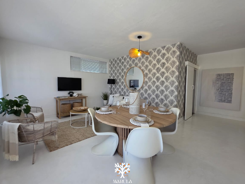 Bright open-plan living and dining area featuring a decorative patterned feature wall, smooth flooring, and a sliding door entrance.