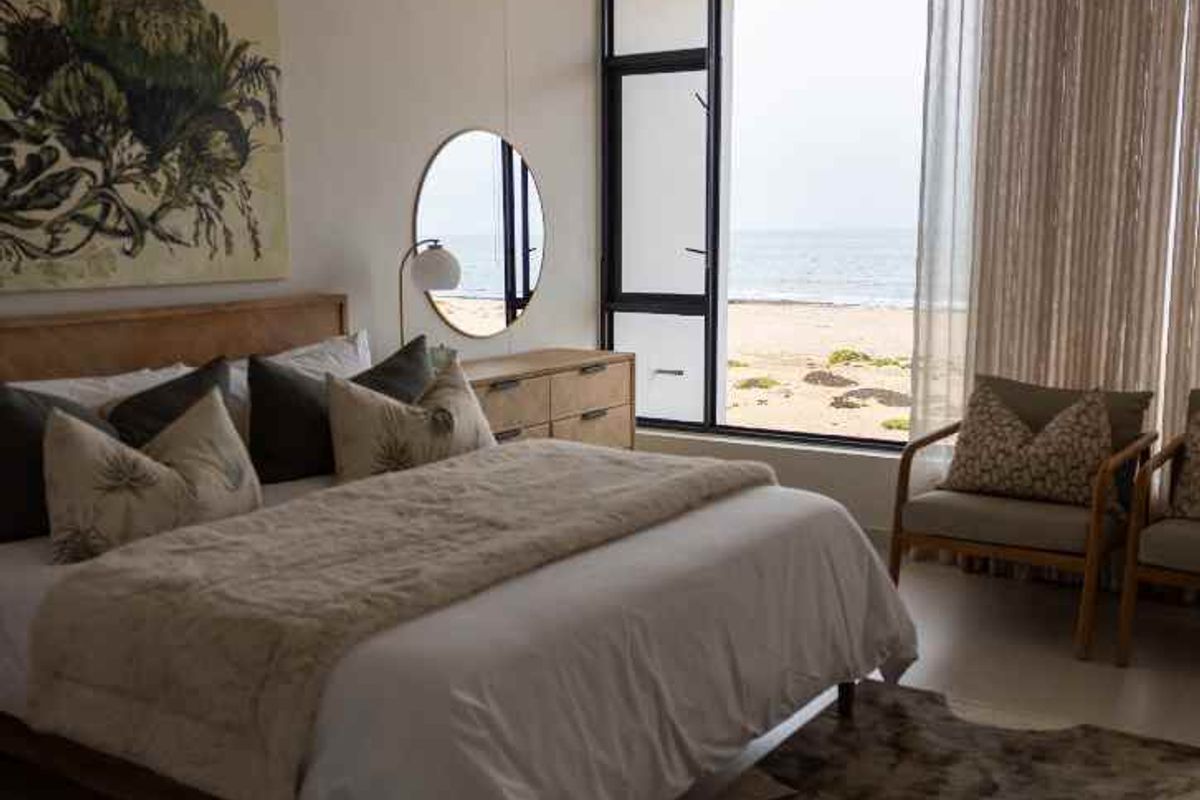 Spacious bedroom featuring large floor-to-ceiling windows with direct ocean views and neutral tiled flooring.