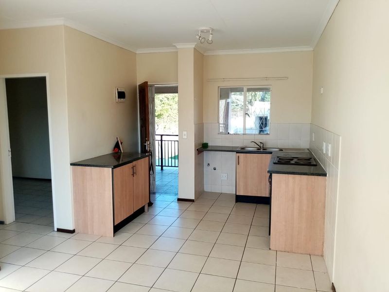 A functional kitchen featuring light wood-finish cabinetry, dark countertops, an electric hob, and tiled flooring, with direct access to an outdoor balcony area.