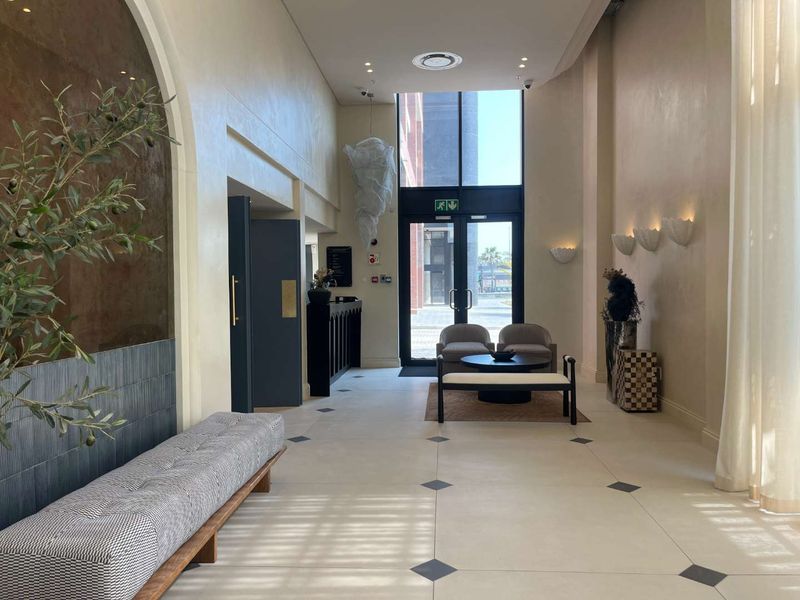 Elegant apartment building entrance lobby featuring high ceilings, tiled flooring with decorative inlays, and modern wall sconce lighting.