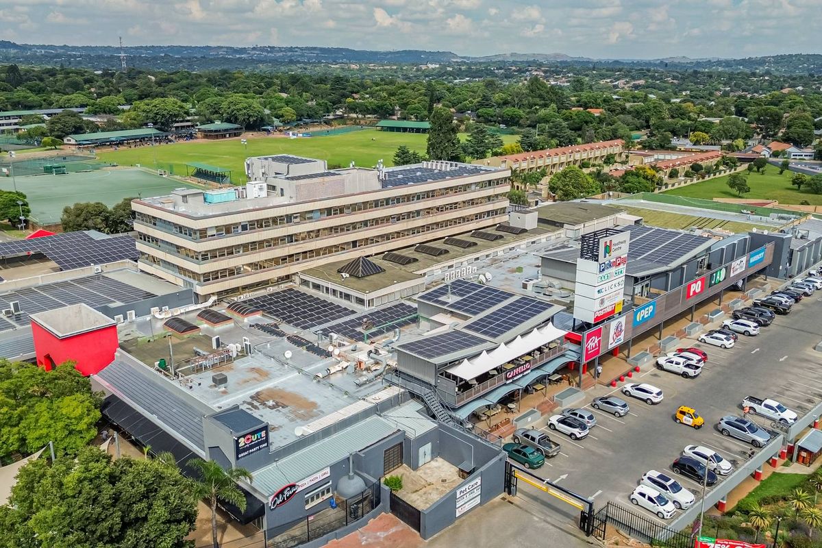 Aerial view of a commercial retail center featuring extensive rooftop solar panel installations, parking facilities, and surrounding landscaped grounds.