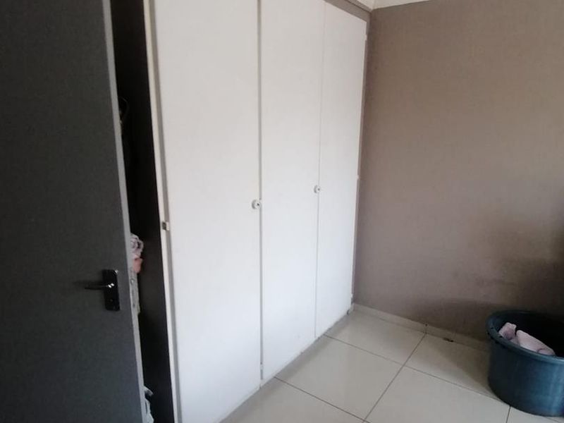 A bedroom featuring neutral wall tones, tiled flooring, and built-in cupboards with white doors.