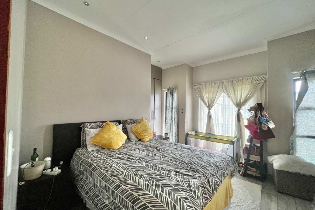 A bedroom featuring built-in cupboards, recessed ceiling lighting, and large windows with curtains, providing a functional and well-lit living space.