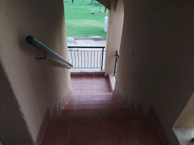 An exterior staircase with tiled steps and metal handrails leading down to a communal garden area.