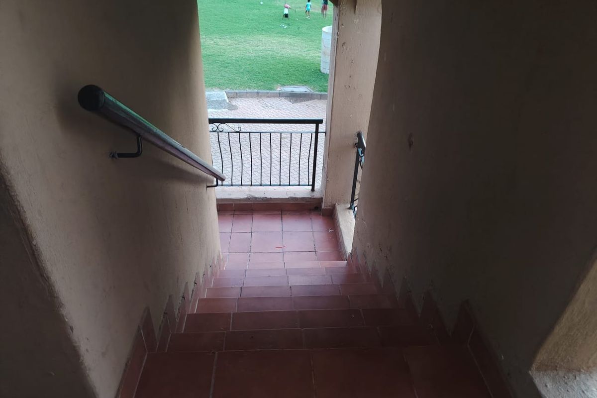 An exterior staircase with tiled steps and metal handrails leading down to a communal garden area.