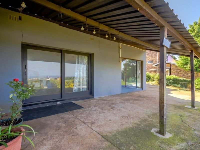 A covered outdoor patio area featuring a corrugated metal roof, timber support posts, and sliding glass door access to the interior.