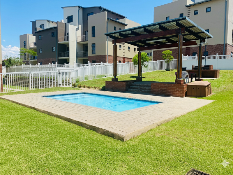 Communal outdoor area featuring a swimming pool, brick-paved surround, and a covered timber pergola with a built-in braai facility.