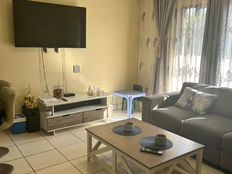 A comfortable living room featuring tiled flooring and a sliding glass door with security gate, providing natural light and access to the exterior.