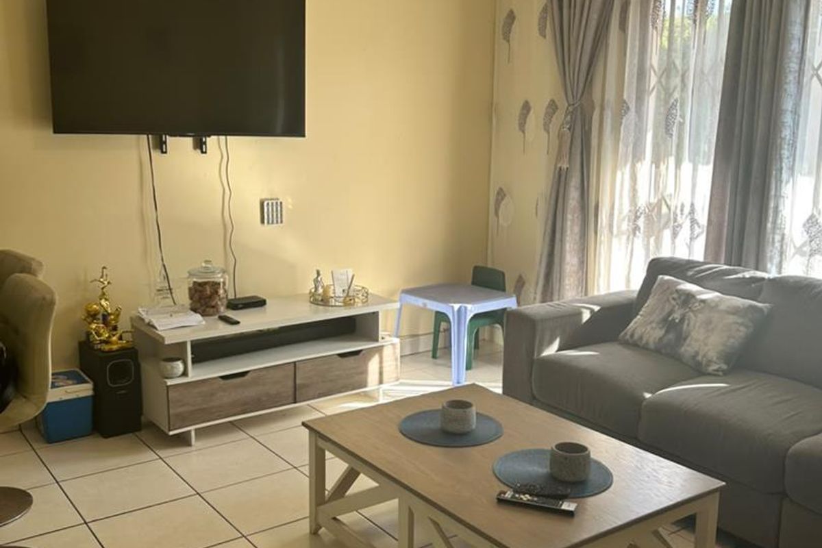 A comfortable living room featuring tiled flooring and a sliding glass door with security gate, providing natural light and access to the exterior.