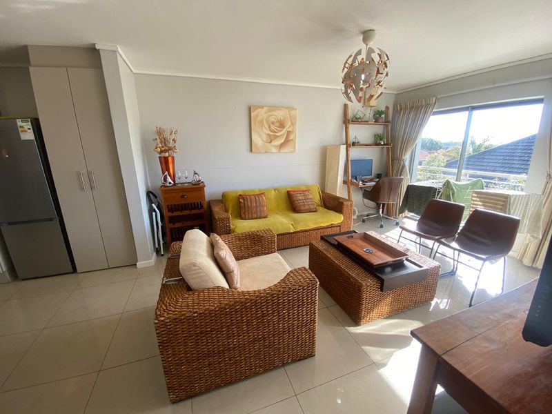 A bright living room featuring large format floor tiles, a built-in storage cupboard, and a sliding glass door leading to an outdoor balcony area.