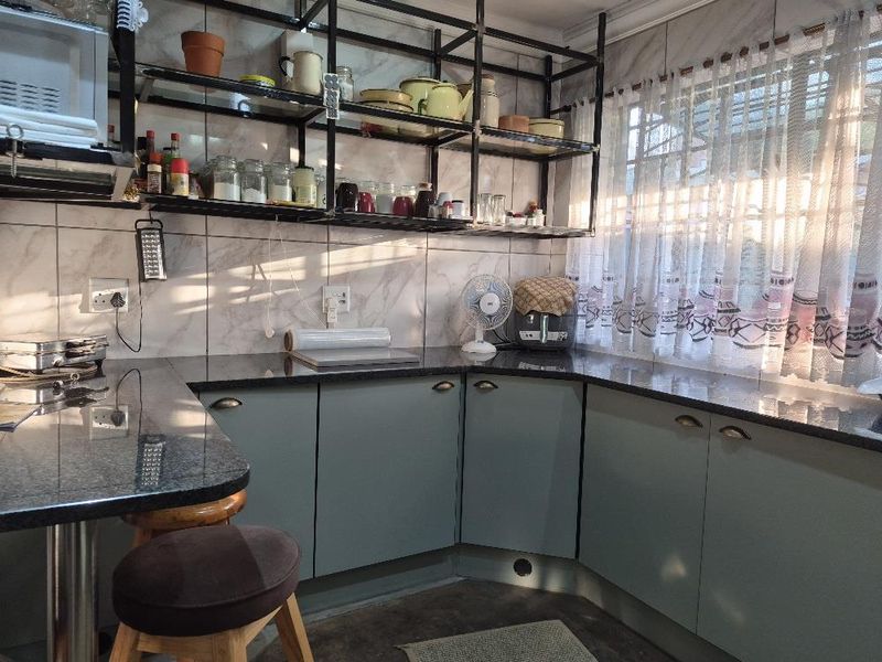 A functional kitchen featuring granite countertops, ample built-in cabinetry, and a tiled backsplash, illuminated by natural light through a window with security bars.