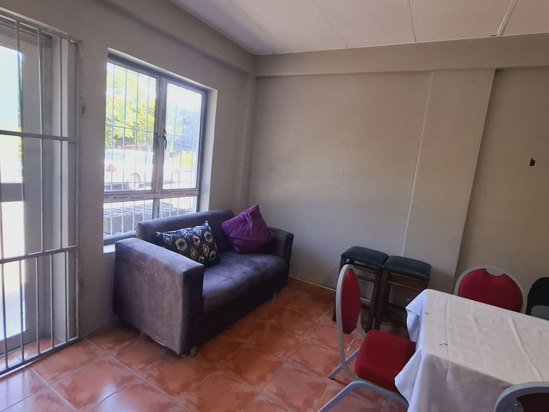 A functional living area featuring tiled flooring, security gate access, and burglar bars on the windows, offering a basic layout for office or commercial use.