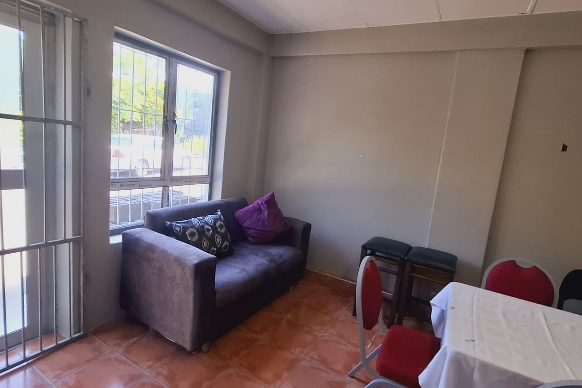 A functional living area featuring tiled flooring, security gate access, and burglar bars on the windows, offering a basic layout for office or commercial use.