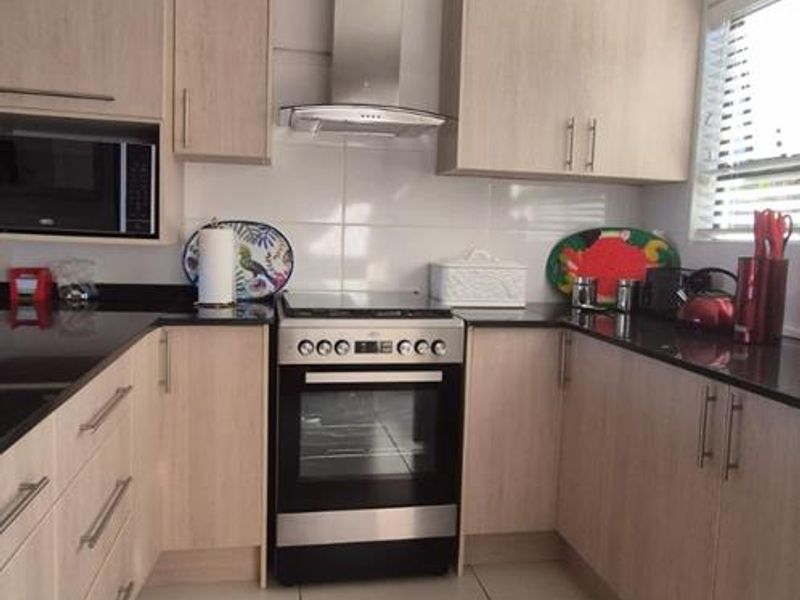 A well-maintained kitchen featuring light wood cabinetry, granite countertops, stainless steel appliances, and neutral tiled flooring.