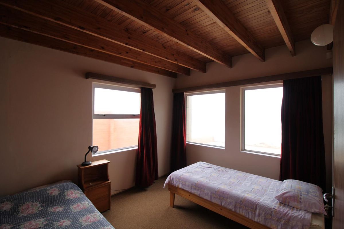A bedroom featuring a timber-beamed ceiling, carpeted flooring, and large windows that provide natural light.