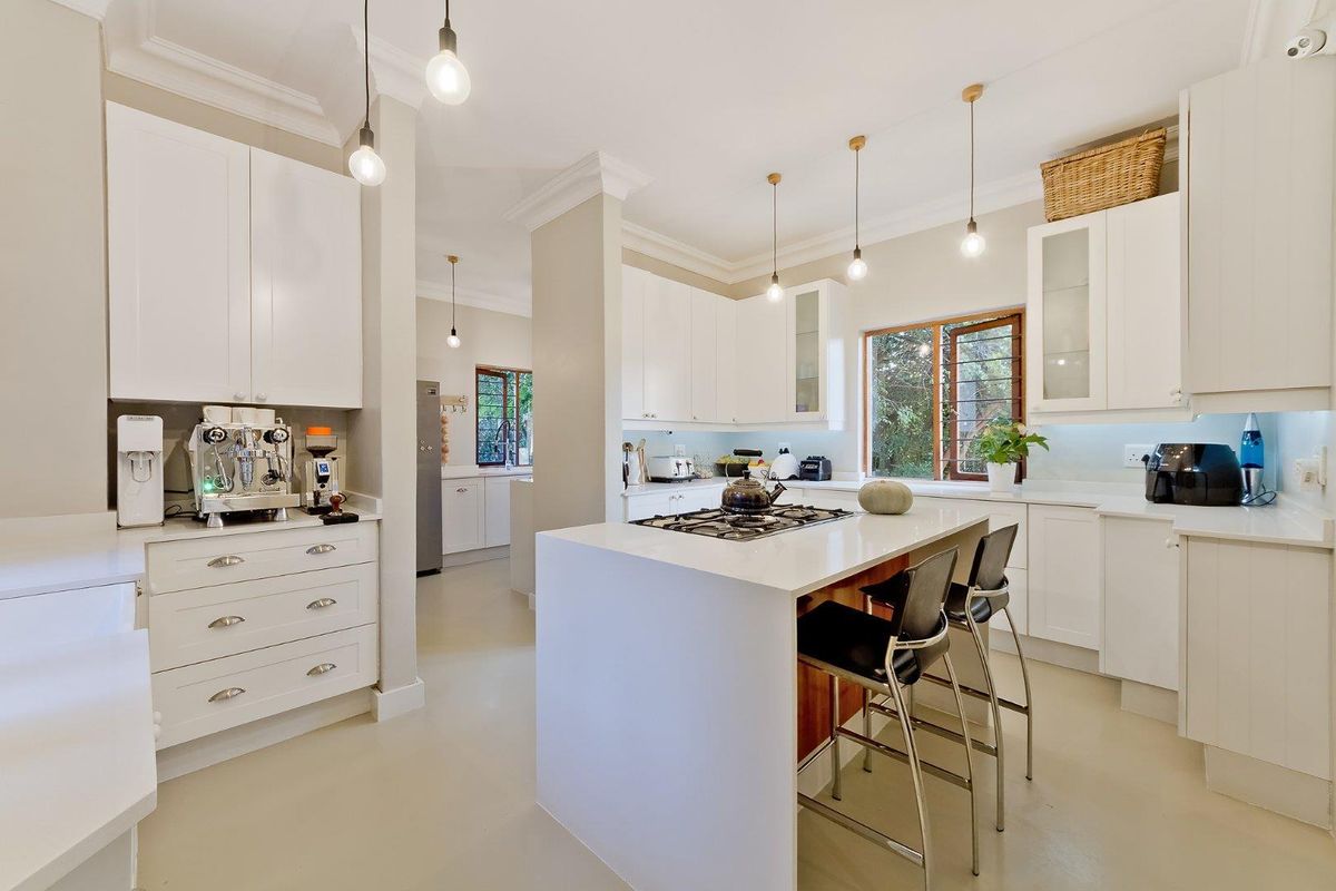 Modern kitchen featuring white cabinetry, stone countertops, a central island with a built-in gas hob, and pendant lighting, with an adjacent scullery area.