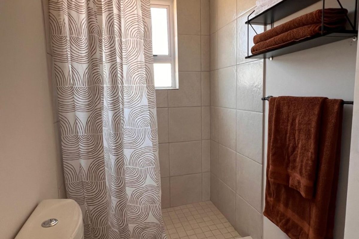 A compact bathroom featuring a shower cubicle with a curtain, a standard toilet, and neutral wall and floor tiling.