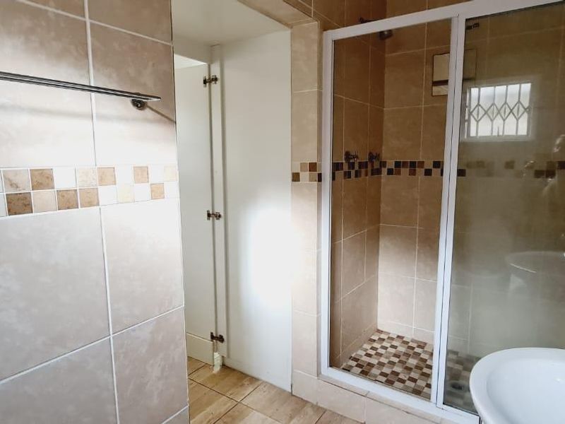 A functional bathroom featuring a shower enclosure, pedestal basin, and neutral tiled finishes throughout.