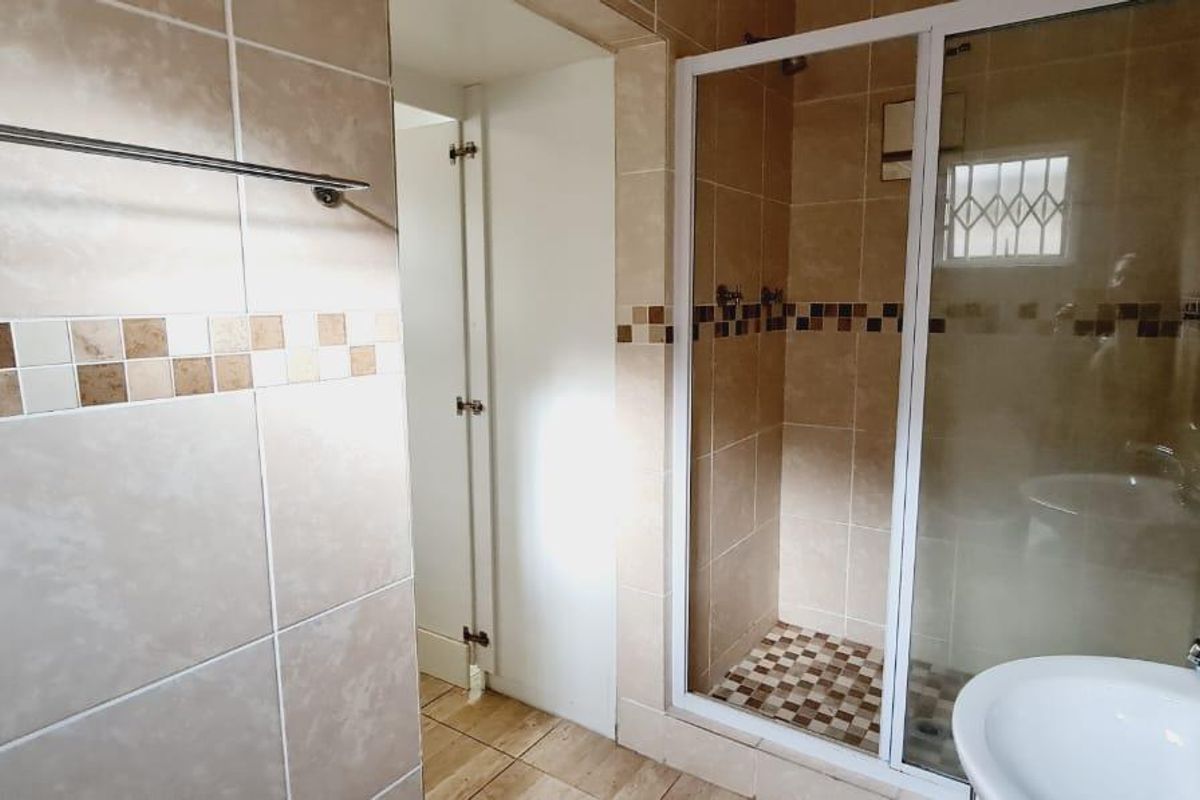 A functional bathroom featuring a shower enclosure, pedestal basin, and neutral tiled finishes throughout.