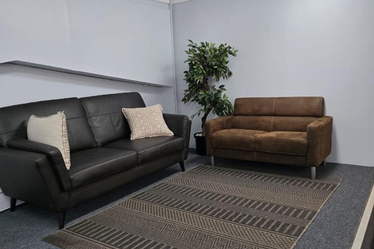 A simple office or lounge area featuring grey carpet flooring, a raised platform section, and basic overhead fluorescent lighting.