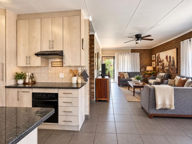 Open-plan living area featuring a modern kitchen with granite countertops, built-in oven, and tiled flooring, flowing into a comfortable lounge with exposed brick accents.