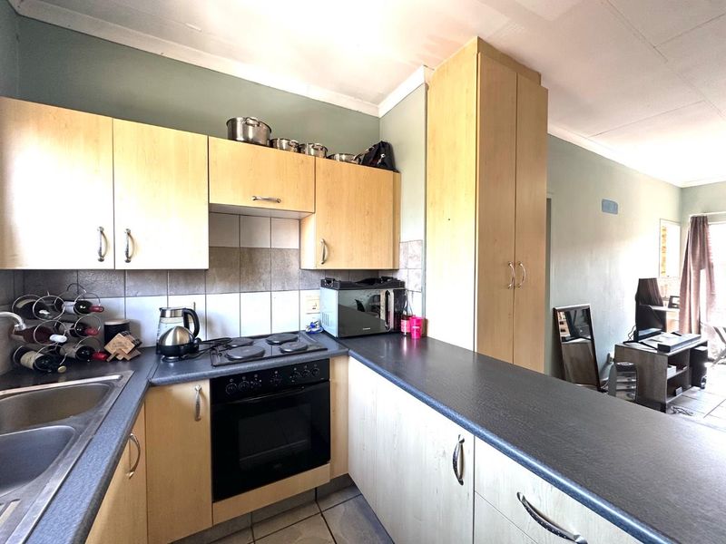 Compact kitchen featuring light wood-finish cabinetry, dark laminate countertops, built-in oven, electric hob, and tiled backsplash, offering functional storage and preparation space.