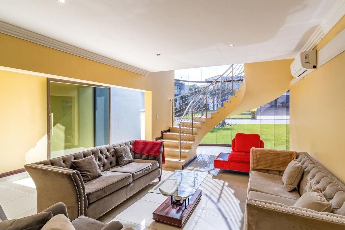 Spacious living area featuring a striking curved staircase with stainless steel balustrades, large glass windows, and tiled flooring.