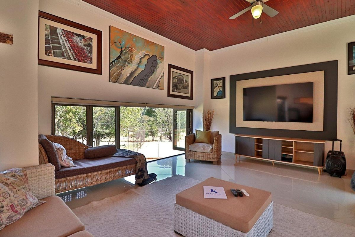 Spacious living room featuring a high timber-paneled ceiling, large sliding glass doors opening to the garden, and a built-in media wall.