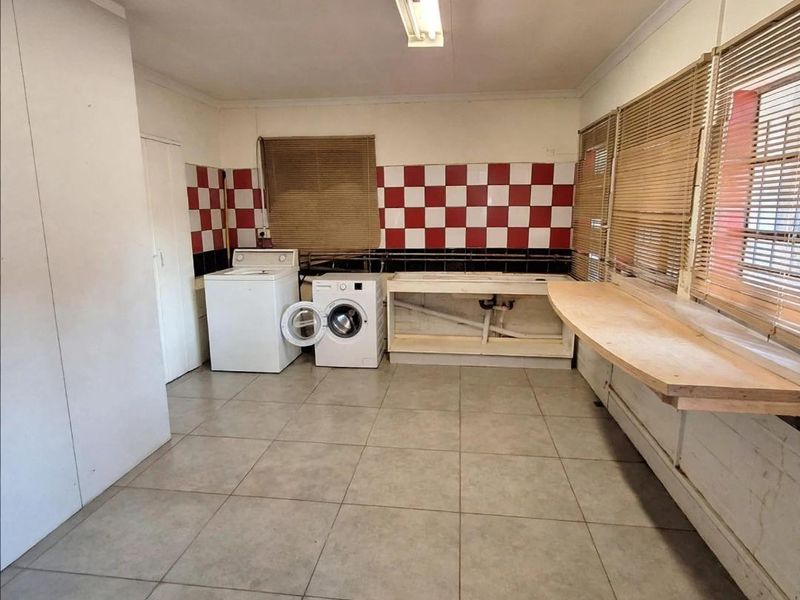 Functional laundry room featuring tiled flooring, a tiled splashback, and built-in counter space with plumbing connections for appliances.