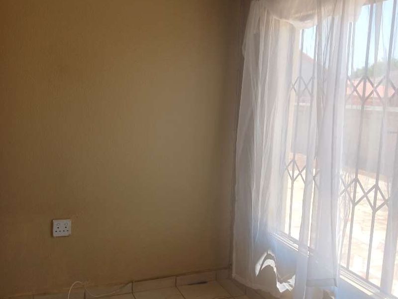 An empty bedroom featuring tiled flooring and security bars on the window, providing a blank canvas for potential renovation or staging.