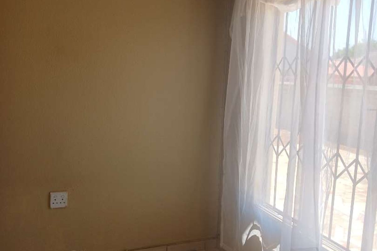 An empty bedroom featuring tiled flooring and security bars on the window, providing a blank canvas for potential renovation or staging.