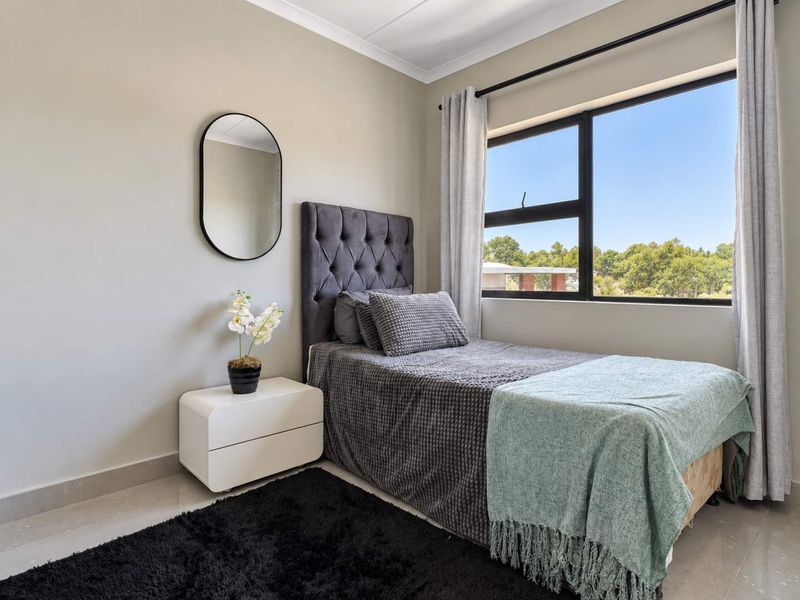 A well-maintained bedroom featuring neutral wall tones, tiled flooring, and a large aluminium-framed window providing natural light and exterior views.