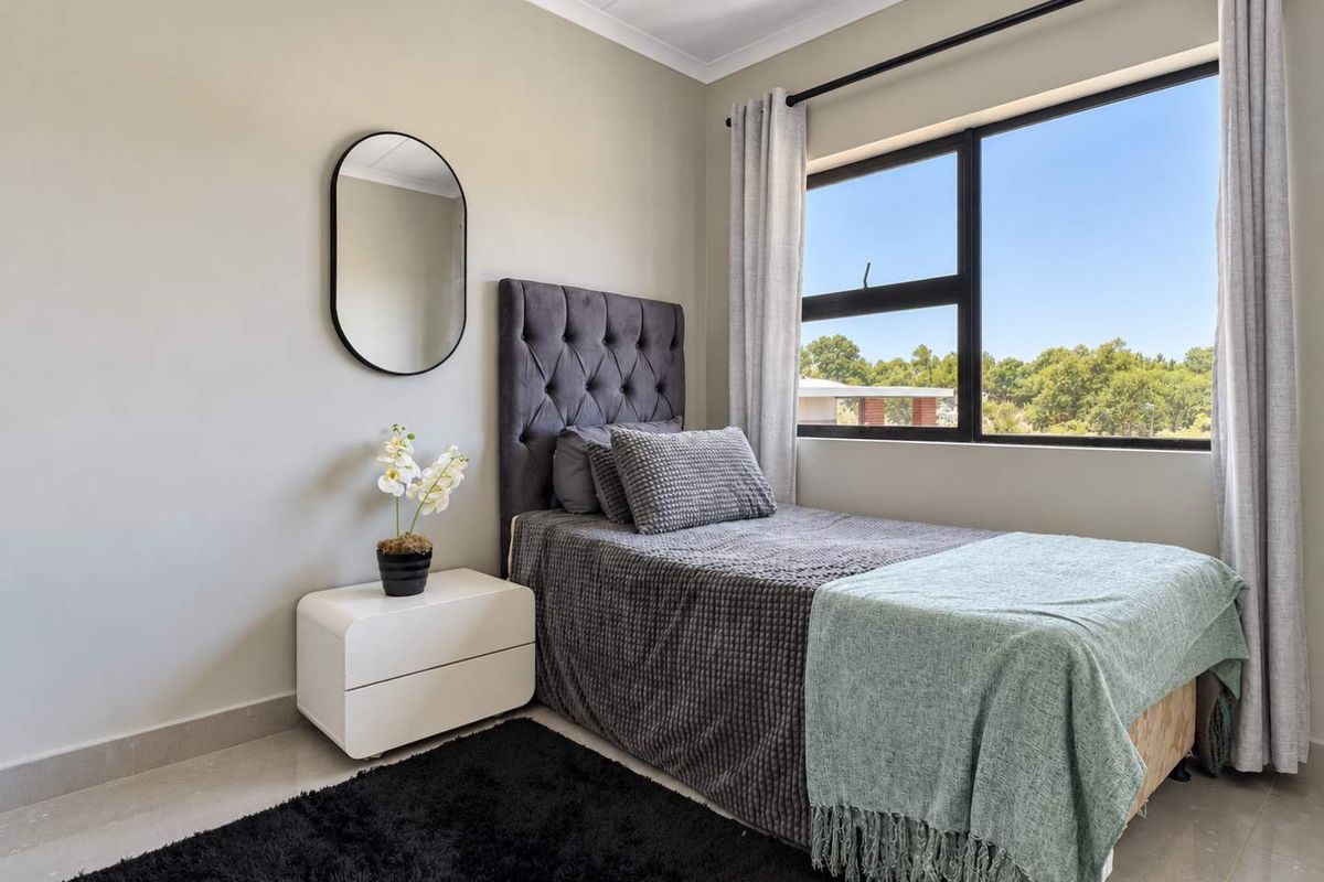 A well-maintained bedroom featuring neutral wall tones, tiled flooring, and a large aluminium-framed window providing natural light and exterior views.