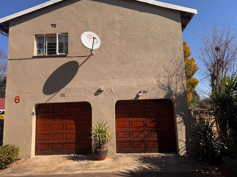 Front elevation of a double-story house featuring a double garage with wooden doors and a paved driveway.