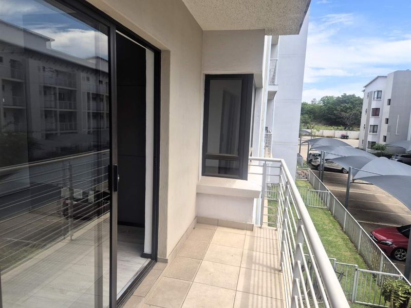 A clean, modern balcony featuring tiled flooring and a metal balustrade, providing an outdoor extension to the apartment living space.