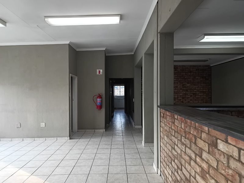 An open-plan office space featuring tiled flooring, exposed brick accents, and functional overhead lighting, presenting a clean and versatile professional environment.