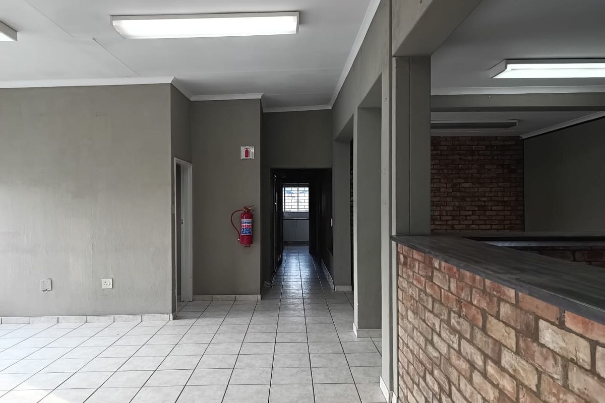 An open-plan office space featuring tiled flooring, exposed brick accents, and functional overhead lighting, presenting a clean and versatile professional environment.