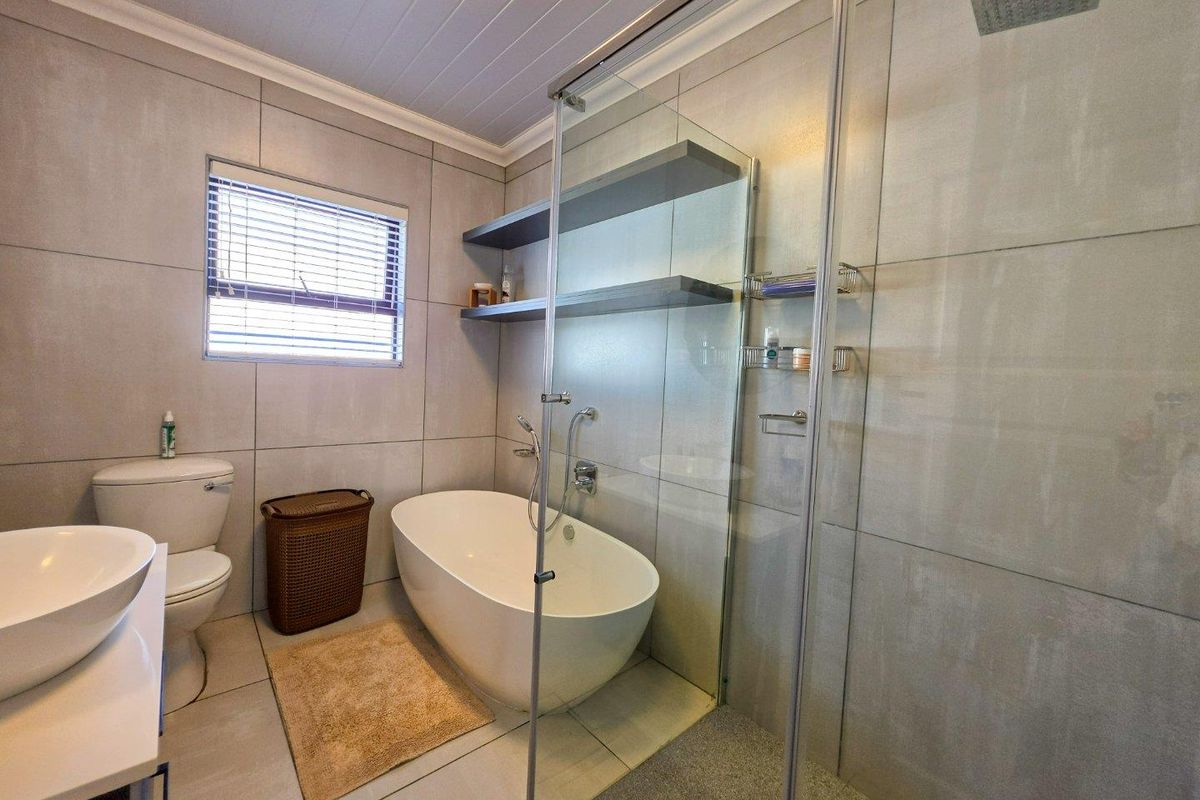 Modern bathroom featuring a freestanding bathtub, glass-enclosed shower with rain head, wall-mounted basin, and neutral floor-to-ceiling tiling.