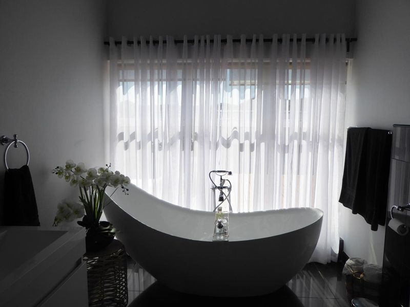 Modern bathroom featuring a sleek freestanding bathtub with floor-mounted faucet, set against a large window with sheer curtains.