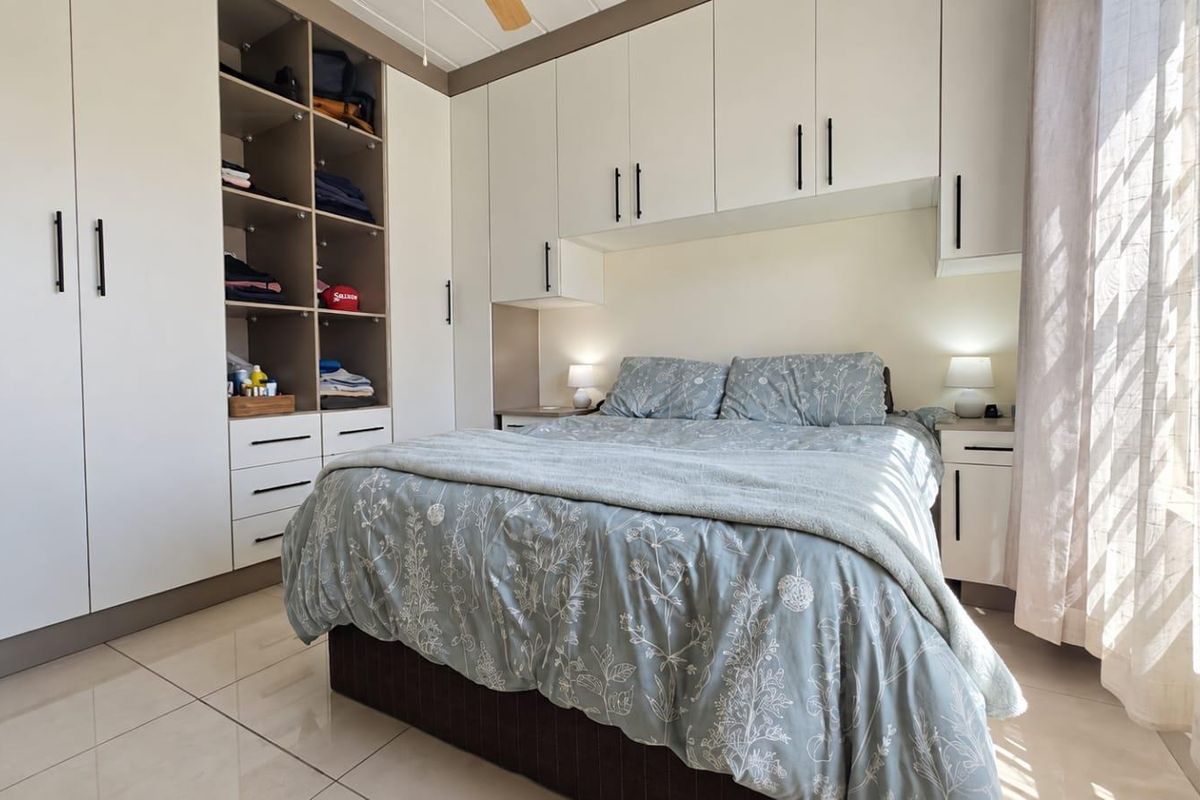 A well-maintained bedroom featuring extensive built-in cabinetry, tiled flooring, and a ceiling fan, offering ample storage and a bright, functional living space.