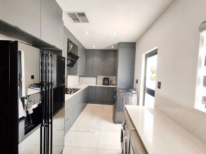 Modern kitchen featuring sleek grey cabinetry, stone countertops, a gas hob with extractor fan, and integrated laundry space with tiled flooring.