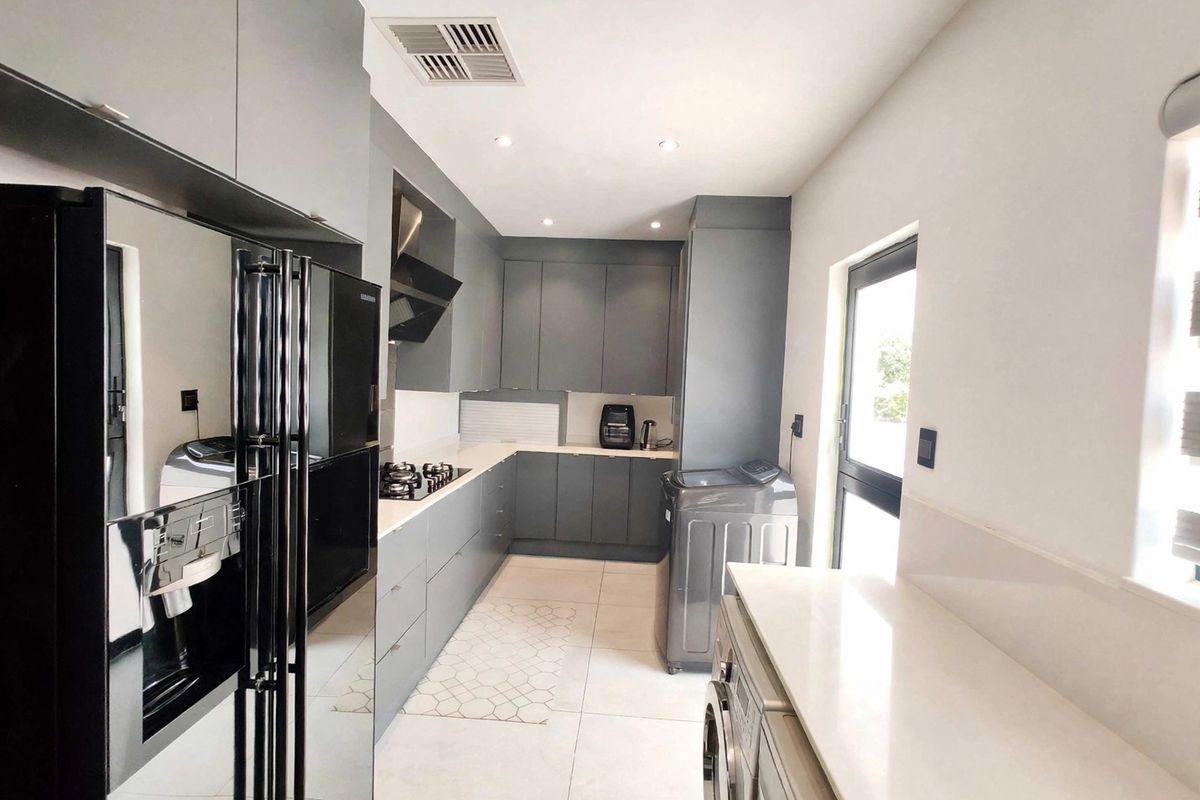 Modern kitchen featuring sleek grey cabinetry, stone countertops, a gas hob with extractor fan, and integrated laundry space with tiled flooring.